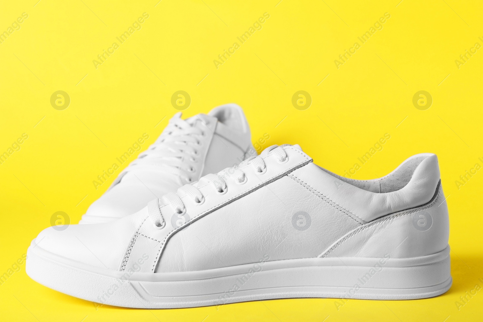 Photo of Pair of stylish white sneakers on yellow background