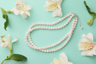 Flat lay composition with elegant pearl necklace and beautiful flowers on turquoise background