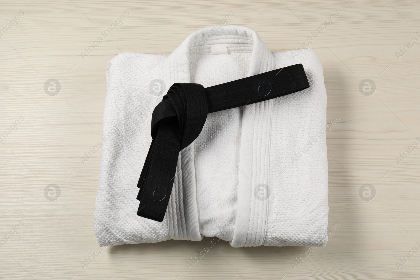 Photo of Black karate belt and white kimono on wooden background, top view