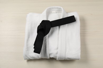 Black karate belt and white kimono on wooden background, top view