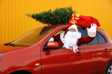 Photo of Authentic Santa Claus with fir tree and bag full of presents driving car against yellow background
