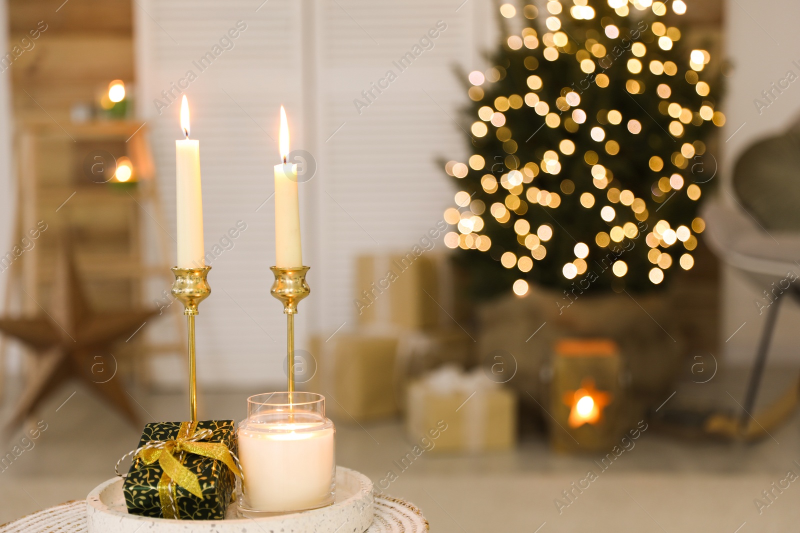 Photo of Burning candles and Christmas gift box on tray indoors. Space for text