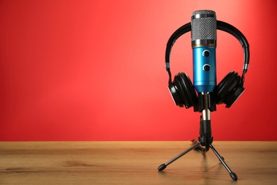 Microphone and modern headphones on wooden table against red background, space for text