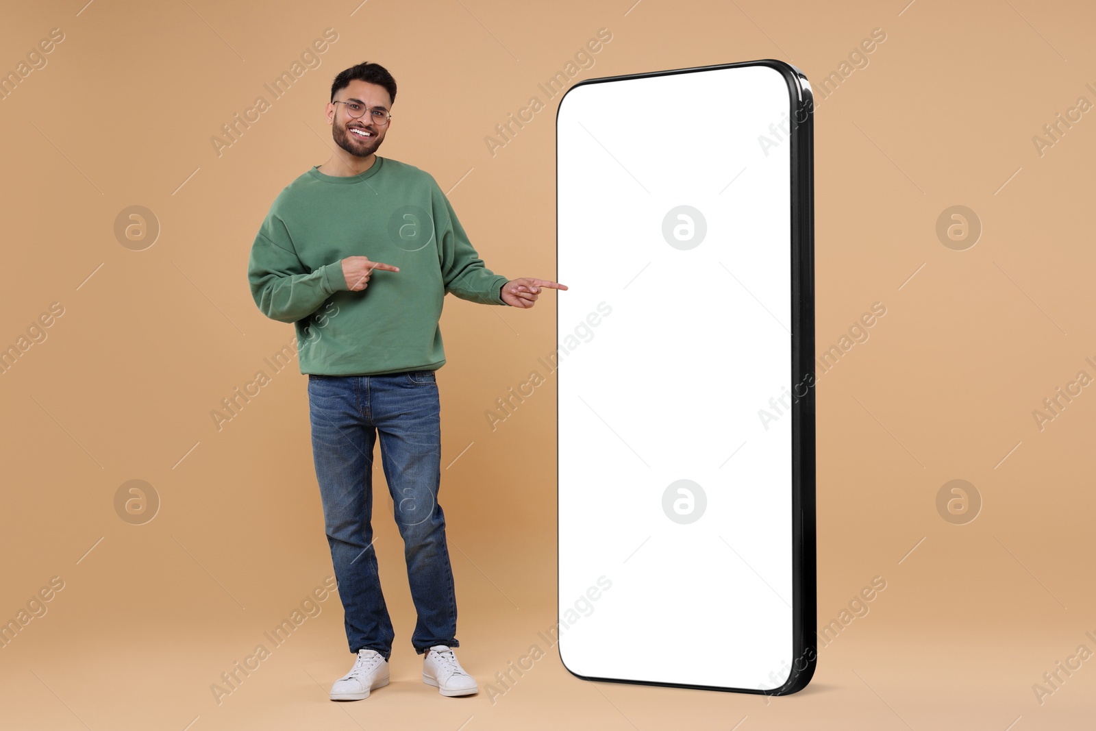 Image of Man pointing at huge mobile phone with empty screen on dark beige background. Mockup for design