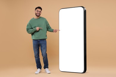 Man pointing at huge mobile phone with empty screen on dark beige background. Mockup for design