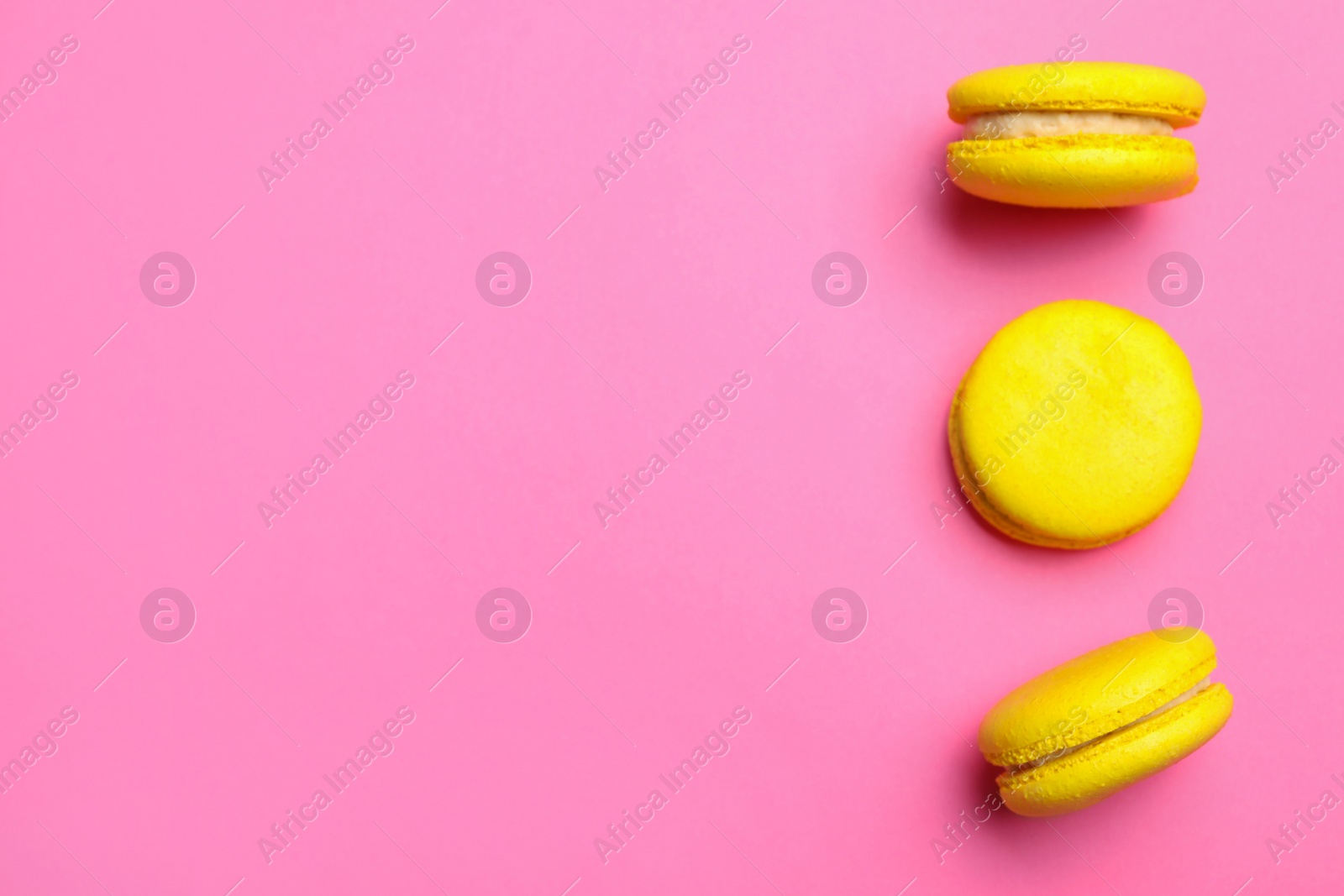 Photo of Delicious yellow macarons on pink background, flat lay. Space for text