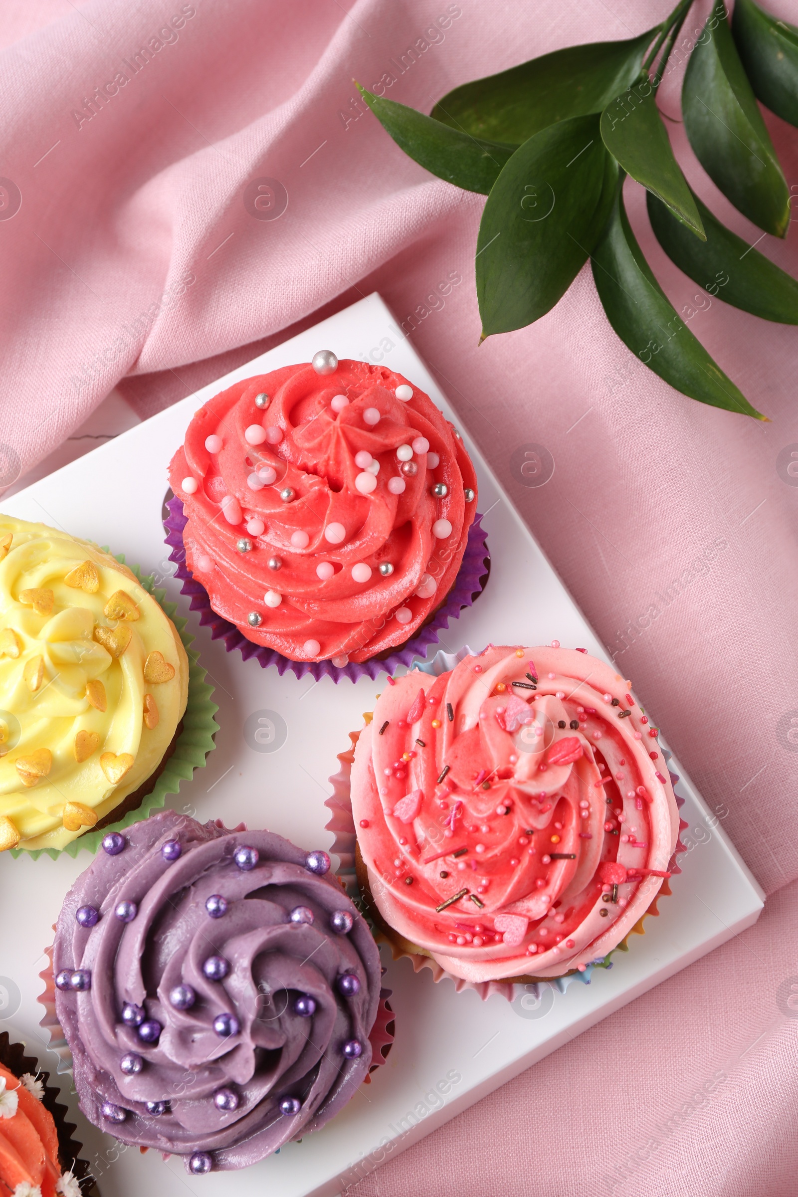 Photo of Delicious cupcake with bright cream on pink fabric, top view