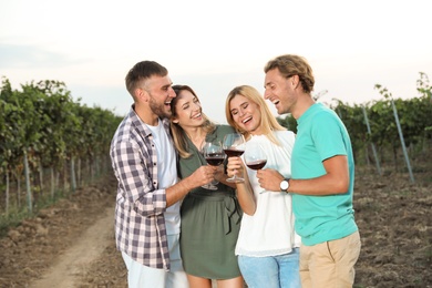 Friends holding glasses of wine and having fun on vineyard picnic