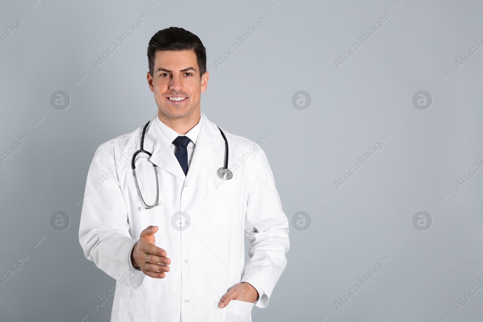 Photo of Happy male doctor offering handshake on light grey background. Space for text