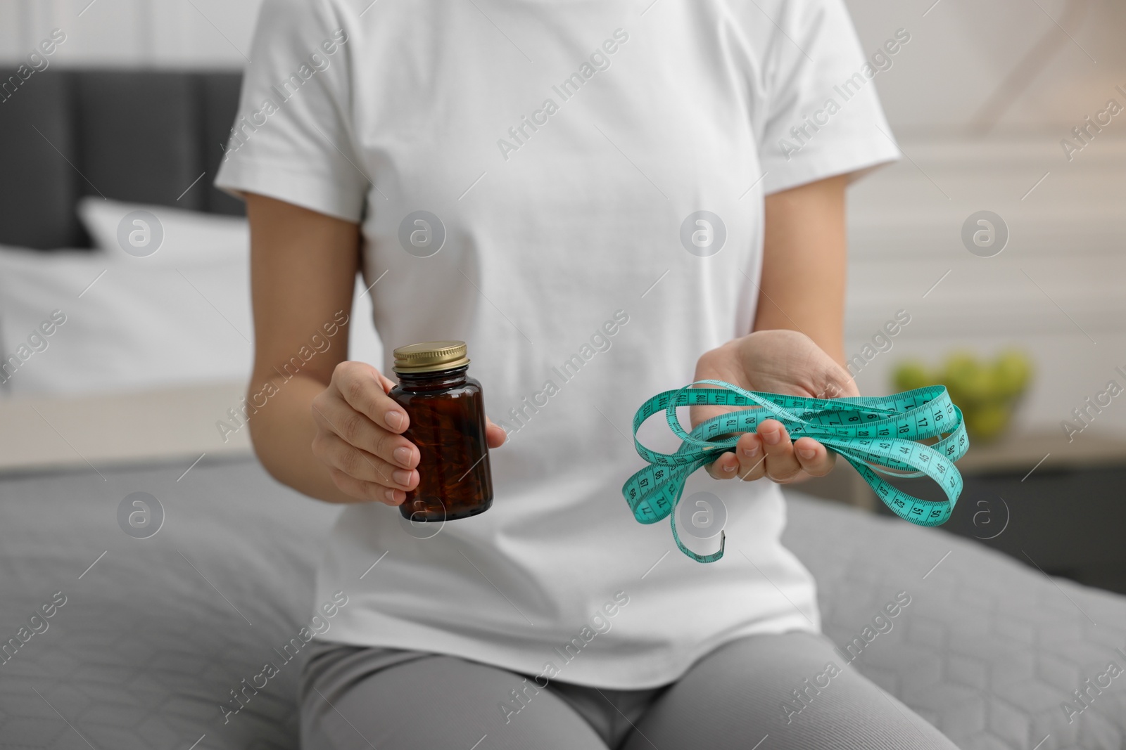 Photo of Woman with pills and measuring tape on bed in room, closeup. Weight loss