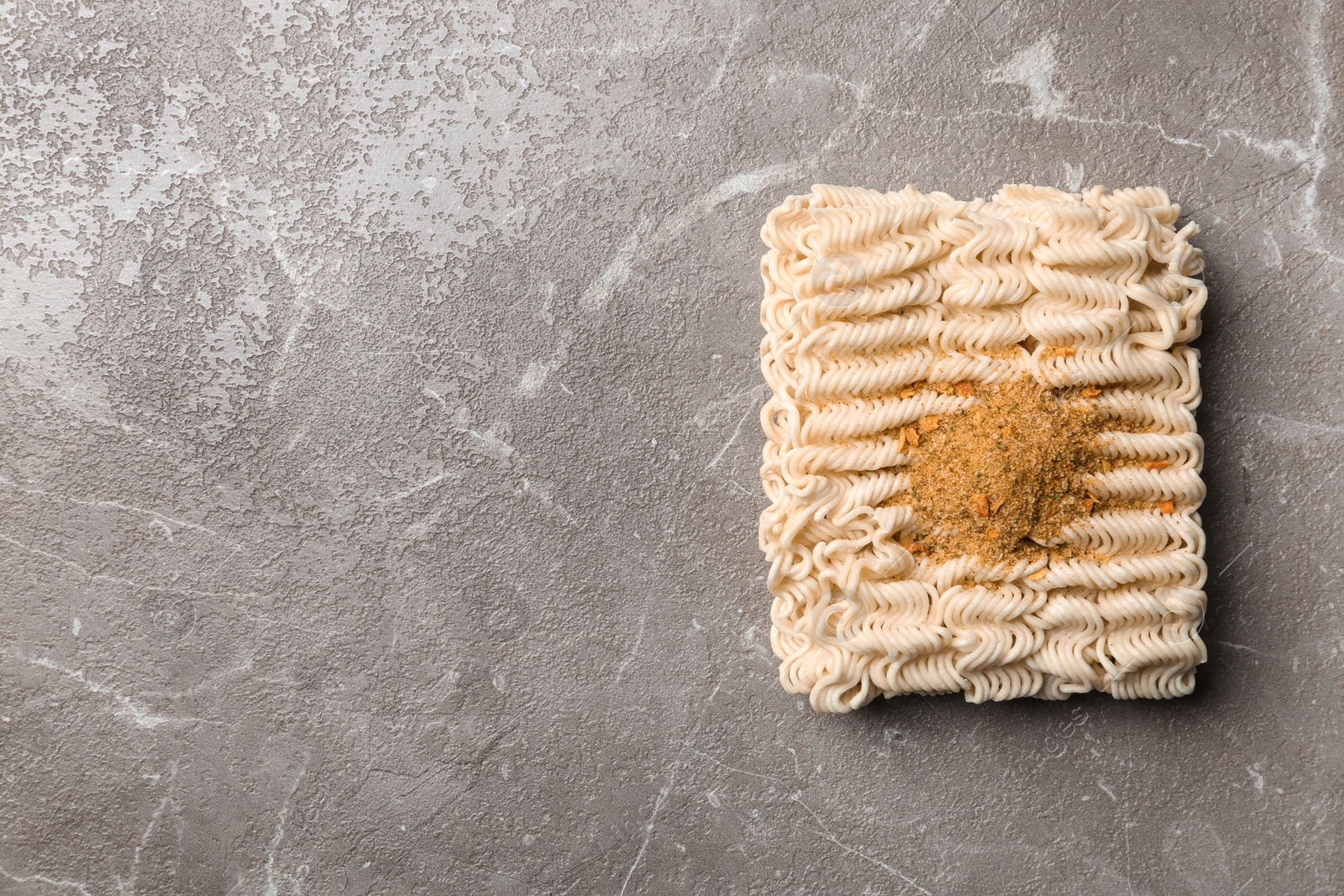 Photo of Block of quick cooking noodles with spices on color background, top view. Space for text