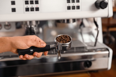 Photo of Barista holding portafilter with coffee beans near machine, closeup. Space for text