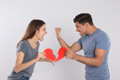 Couple with torn paper heart quarreling on light background. Relationship problems