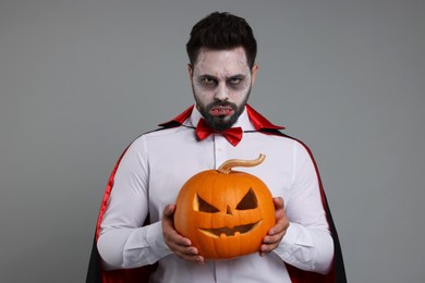 Man in scary vampire costume with fangs and carved pumpkin on light grey background. Halloween celebration