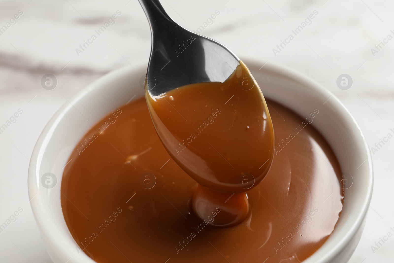 Photo of Taking yummy salted caramel with spoon from bowl on table, closeup