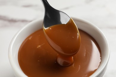 Taking yummy salted caramel with spoon from bowl on table, closeup