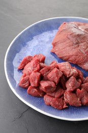 Photo of Plate with pieces of raw beef meat on grey textured table, closeup