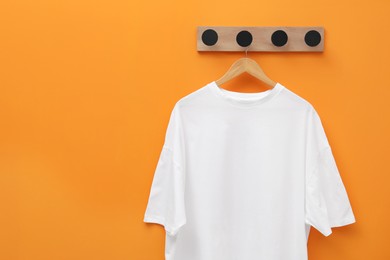 Hanger with white T-shirt on orange wall, space for text