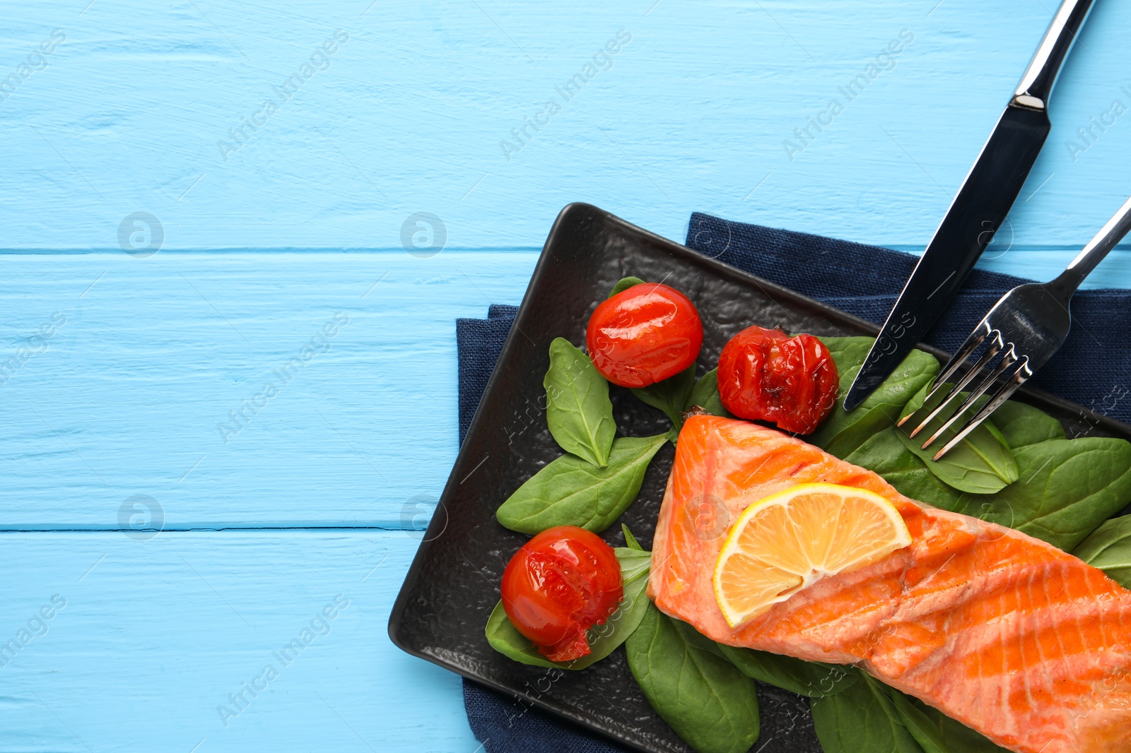 Photo of Tasty grilled salmon with tomatoes, spinach and lemon served on light blue table, top view. Space for text