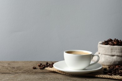 Photo of Cup of aromatic coffee and beans on wooden table. Space for text