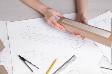 Woman creating packaging design at light wooden table, top view