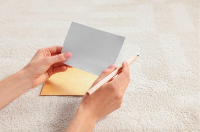 Woman writing message in greeting card on carpet in room, closeup. Space for text