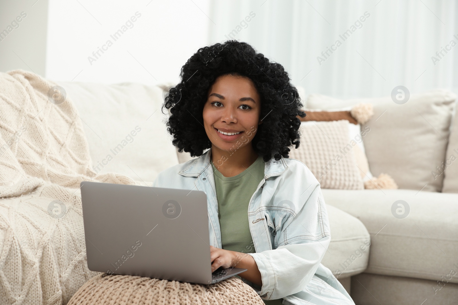 Photo of Happy young woman using laptop on pouf at home