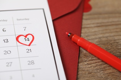 Calendar with marked Valentine's Day and red felt tip pen on wooden table, closeup