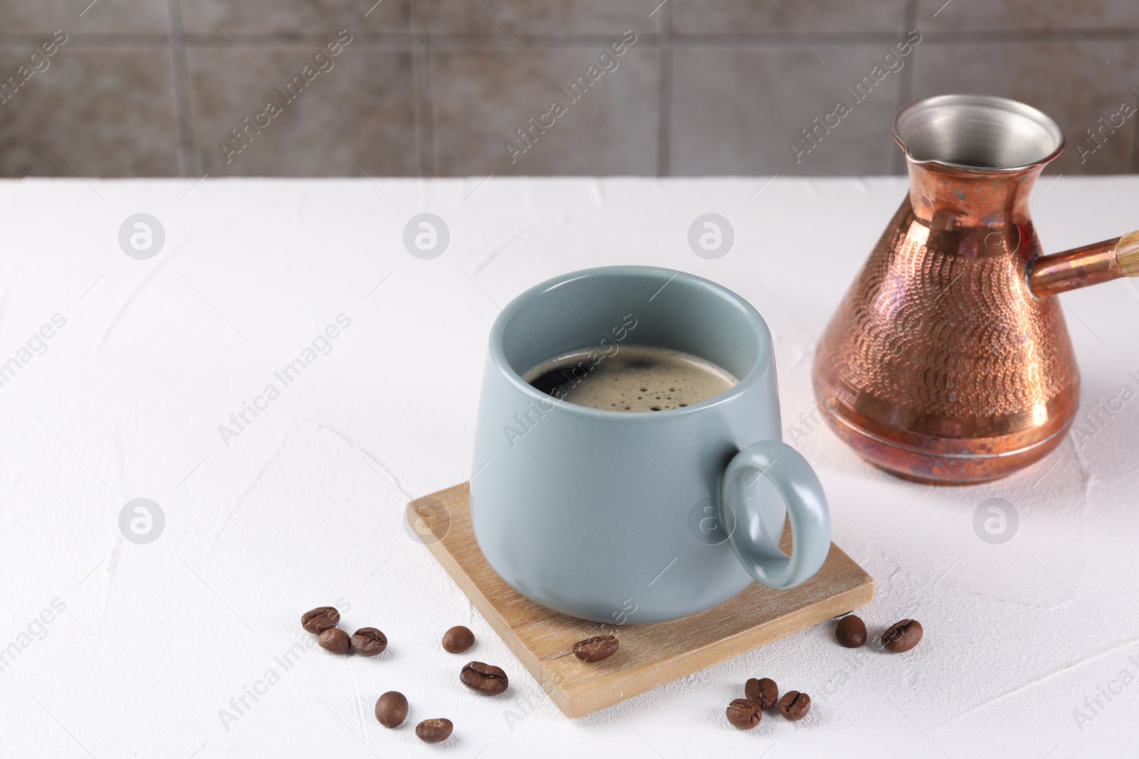 Photo of Delicious coffee in cup, cezve and beans on white textured table. Space for text