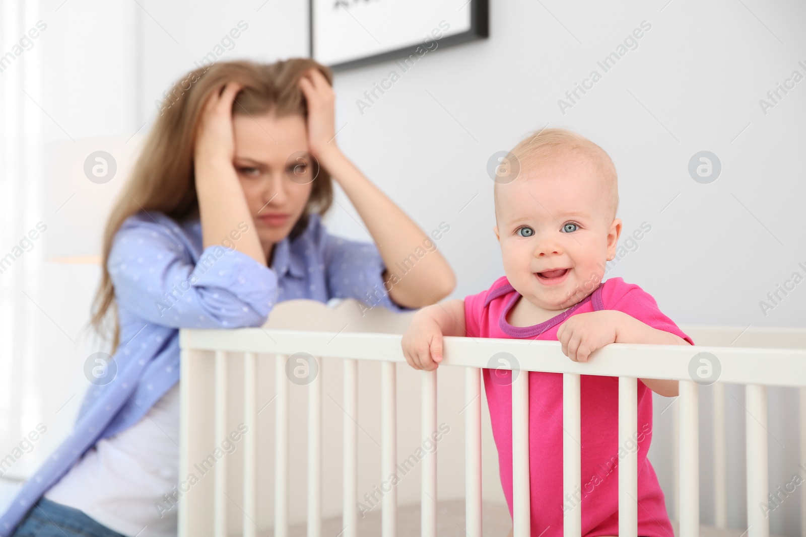 Photo of Young mother suffering from postnatal depression near crib with cute baby at home