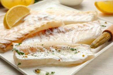 Photo of Fresh raw cod fillets with spices, lemon and brush on white wooden table, closeup