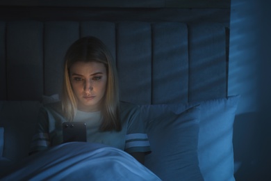 Young woman using smartphone in bed at night. Nomophobia and sleeping disorder problem