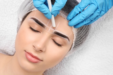 Photo of Cosmetologist preparing young woman for eyebrow permanent makeup procedure, closeup