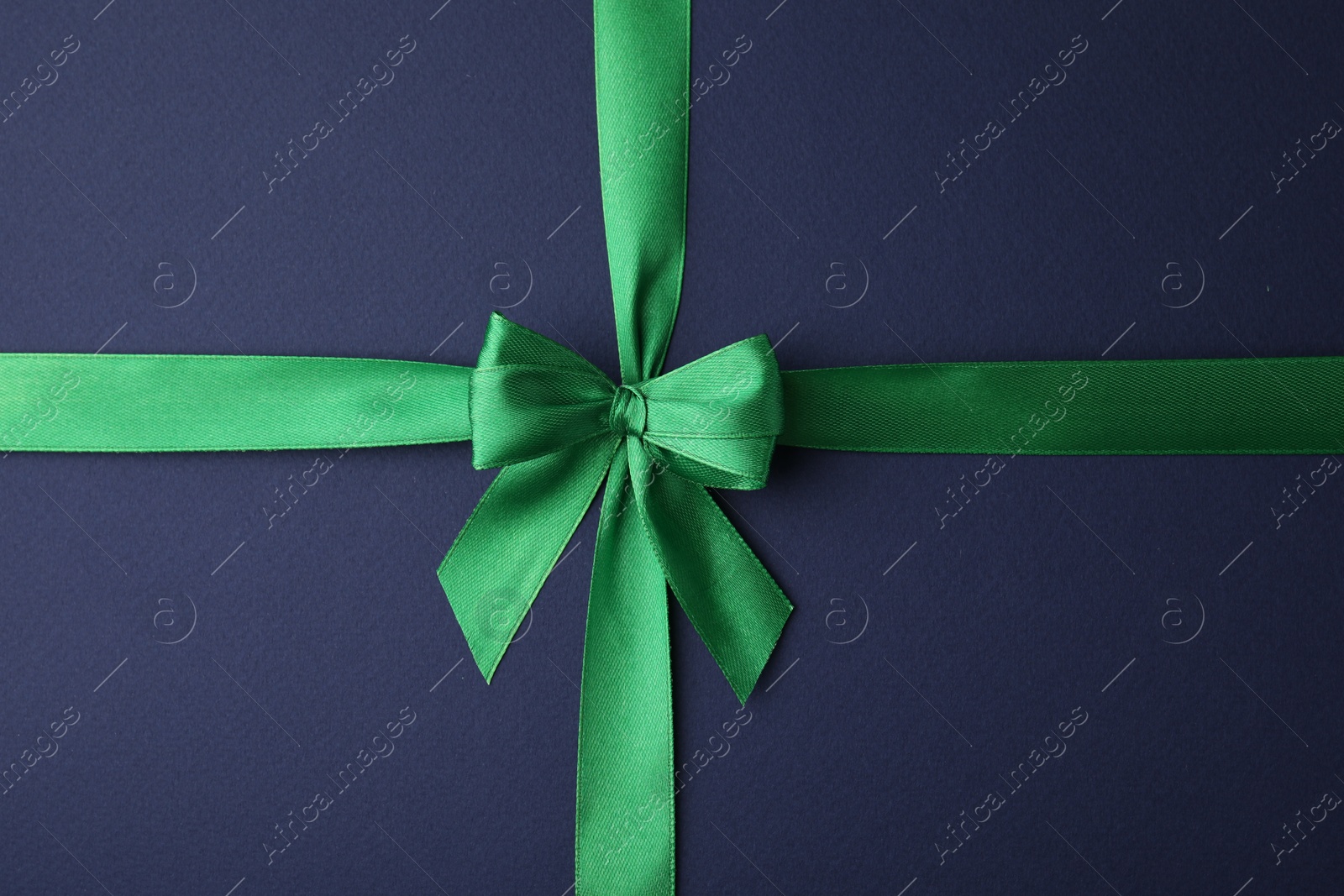 Photo of Green satin ribbon with bow on blue background, top view