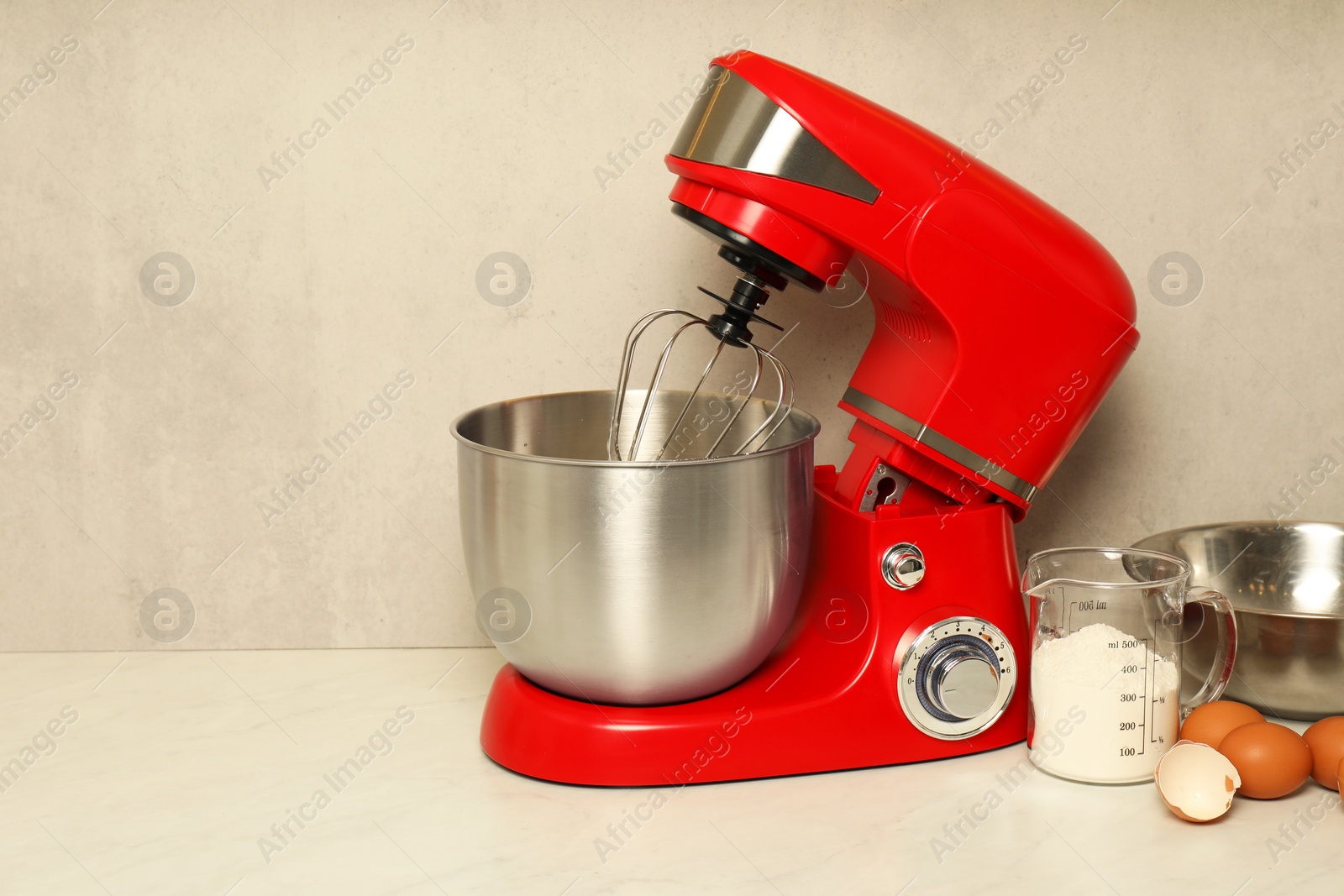 Photo of Modern red stand mixer, eggs, container with flour and bowl on white marble table. Space for text