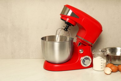 Photo of Modern red stand mixer, eggs, container with flour and bowl on white marble table. Space for text