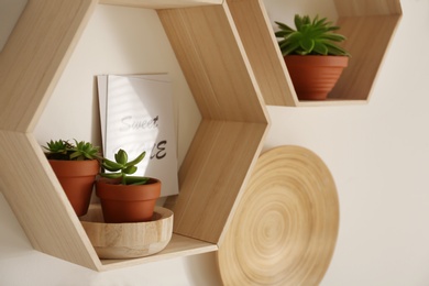 Photo of Hexagon wooden shelves with beautiful plants and decorative elements on light wall