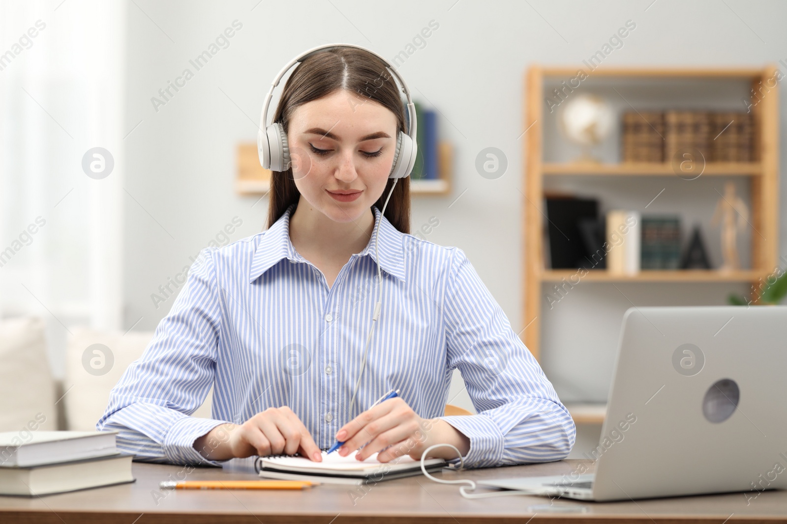 Photo of E-learning. woman taking notes during online lesson at table indoors