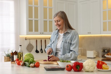 Happy woman cutting onion at table in kitchen