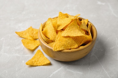 Photo of Tasty mexican nachos chips in wooden bowl on grey table
