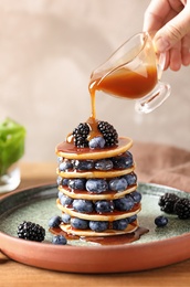 Photo of Woman pouring syrup onto tasty pancakes with berries on plate, closeup