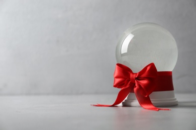 Beautiful Christmas snow globe with red bow on grey table, space for text