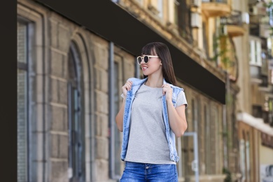 Photo of Young woman in grey t-shirt and denim vest outdoors. Mockup for design