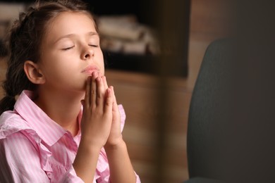 Cute little girl with hands clasped together praying at home. Space for text