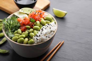 Photo of Delicious poke bowl with lime, fish and edamame beans on black table, space for text