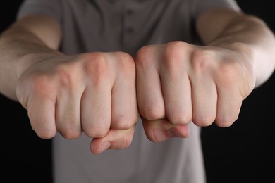 Photo of Man showing fists with space for tattoo on black background, closeup