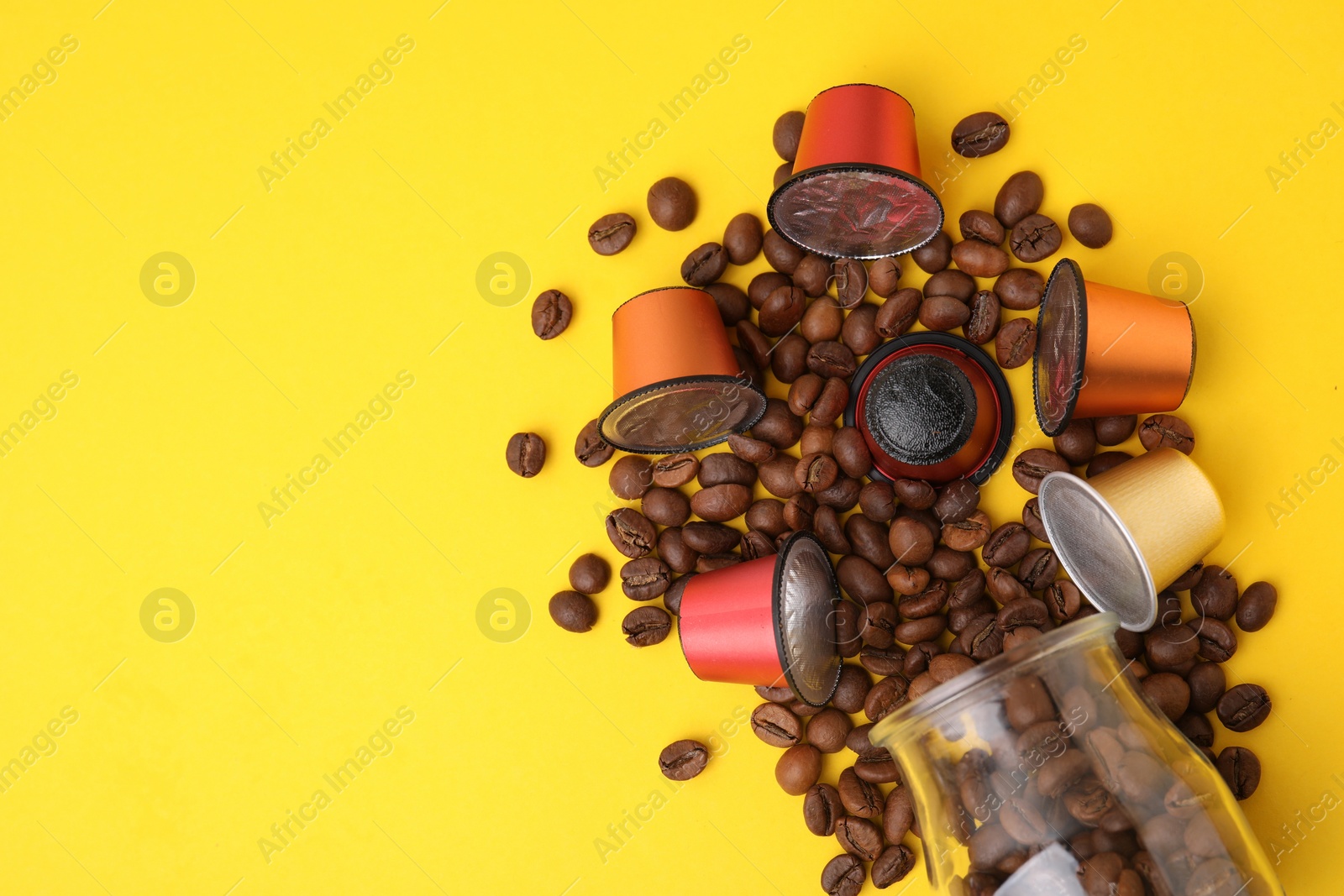 Photo of Many coffee capsules, beans and glass jar on yellow background, flat lay. Space for text