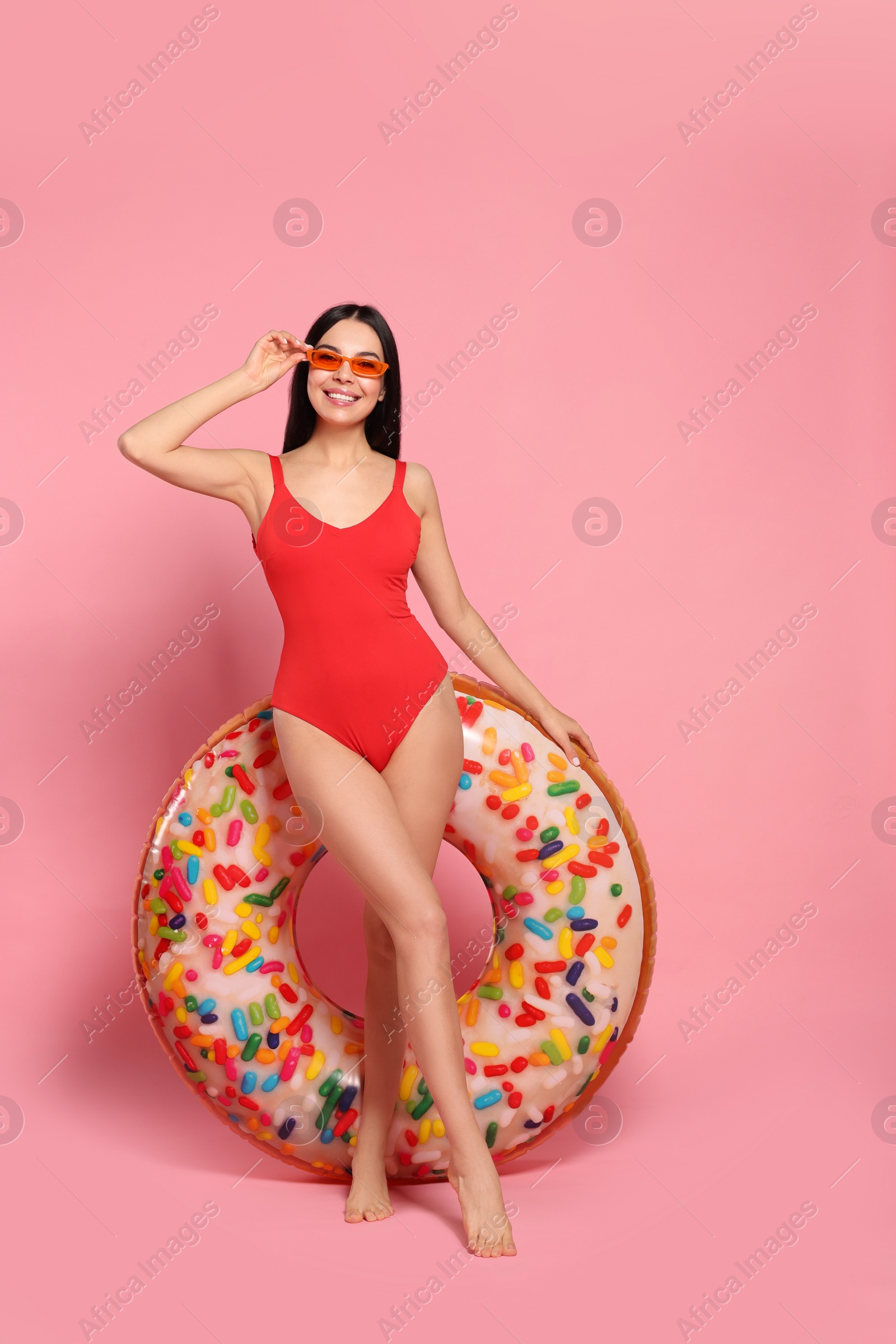 Photo of Young woman with stylish sunglasses holding inflatable ring against pink background