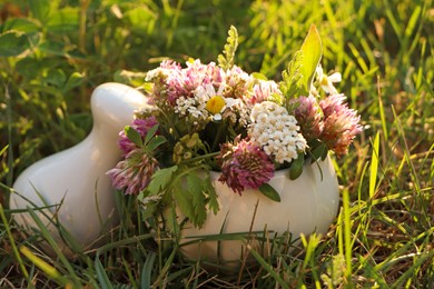 Photo of Ceramic mortar with pestle, different wildflowers and herbs green grass outdoors, closeup