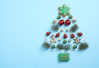 Christmas tree silhouette of fir branches and festive decoration on light blue background, flat lay. Space for text